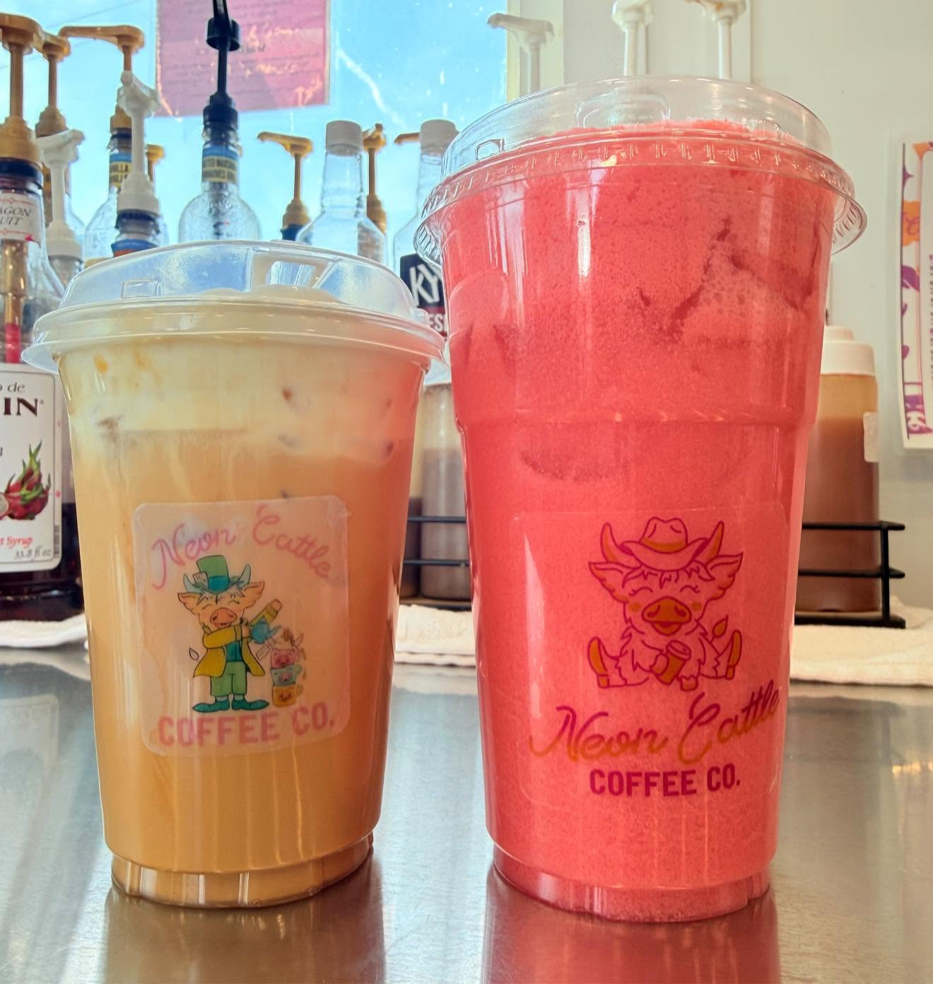An iced latte and a red refresher in labeled Neon Cattle cups on the counter