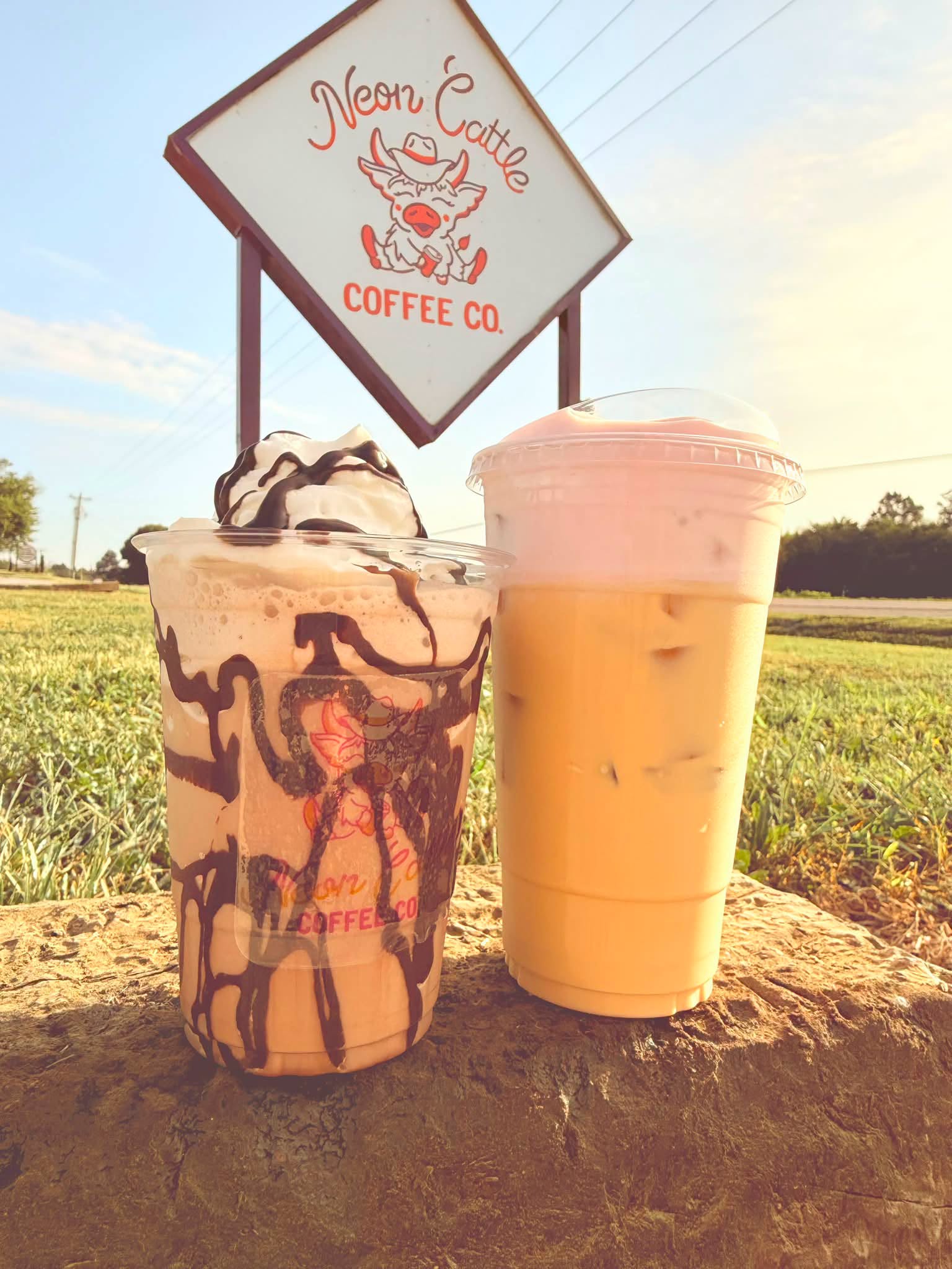 Chocolate-drizzled frappe and an iced latte in front of the Neon Cattle sign