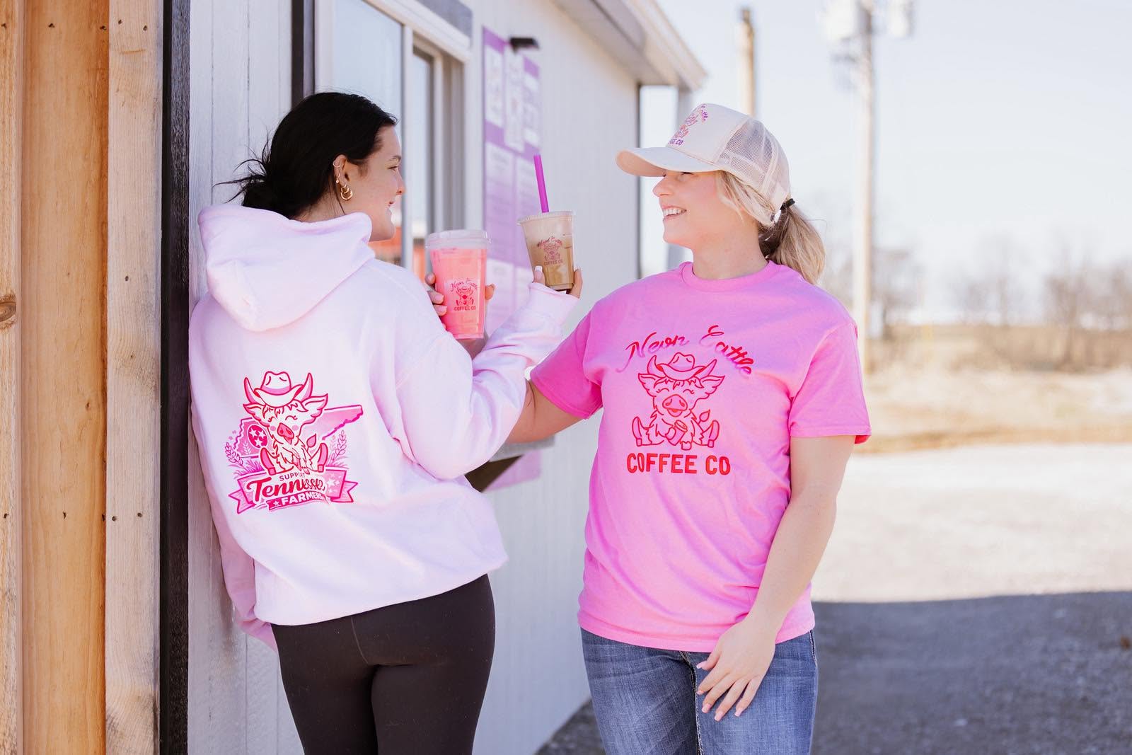 Two customers in Neon Cattle merch toasting their drinks at the stand