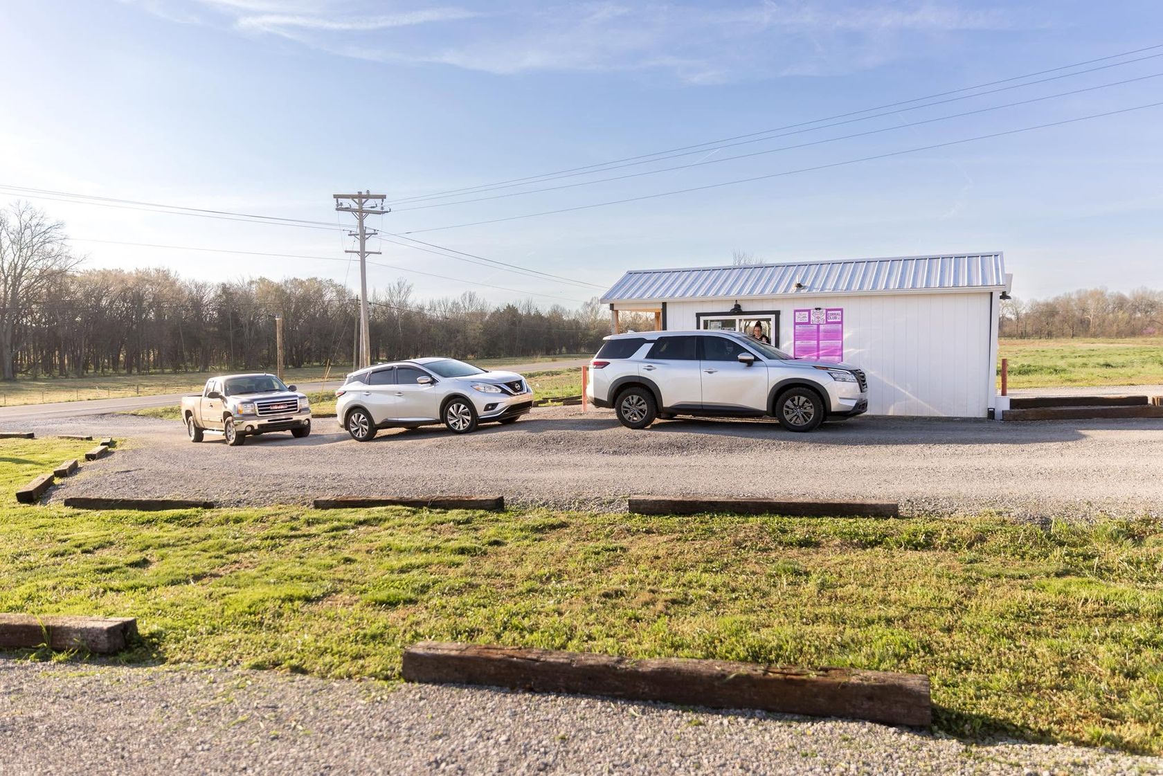 The white Neon Cattle stand with its pink menu board and cars lined up at the drive-thru window